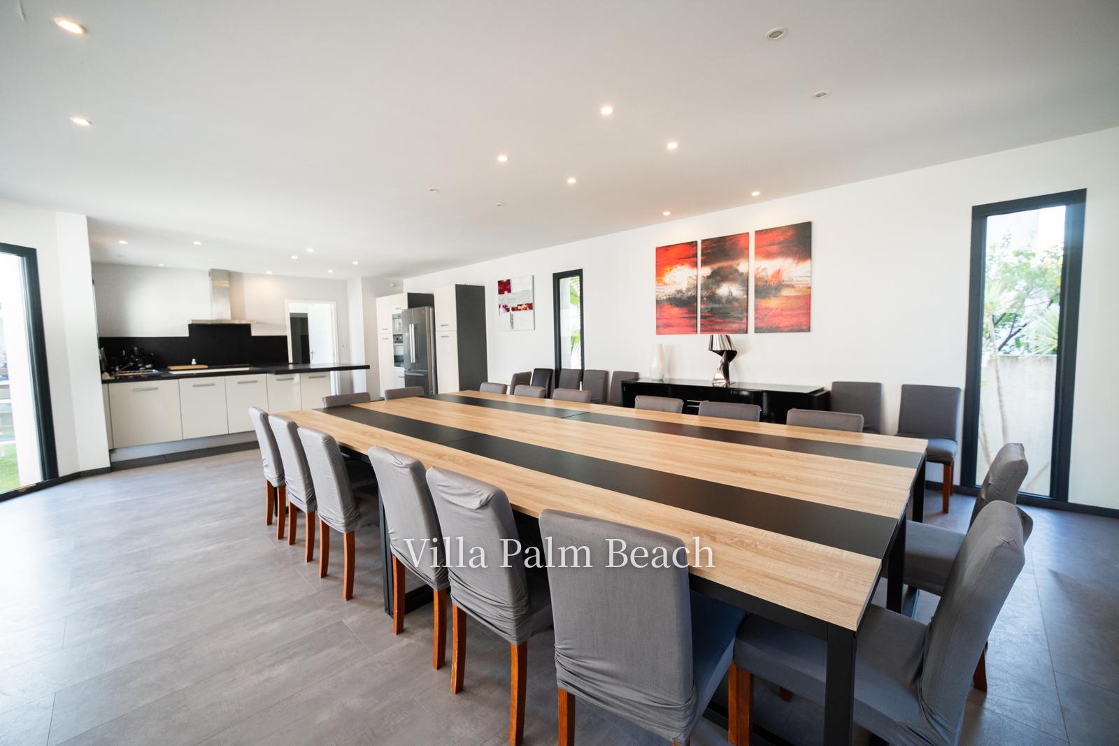 Grande table à manger d'une vingtaine de places, cuisine ouverte au fond